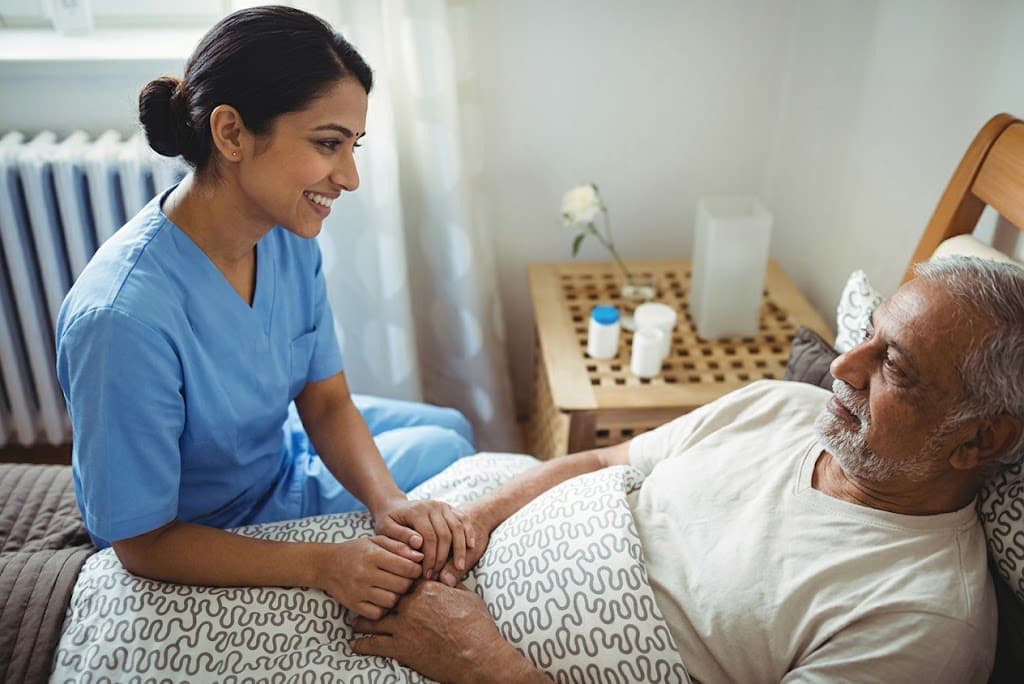 Nurse holding elderly patient's hand providing compassionate palliative care