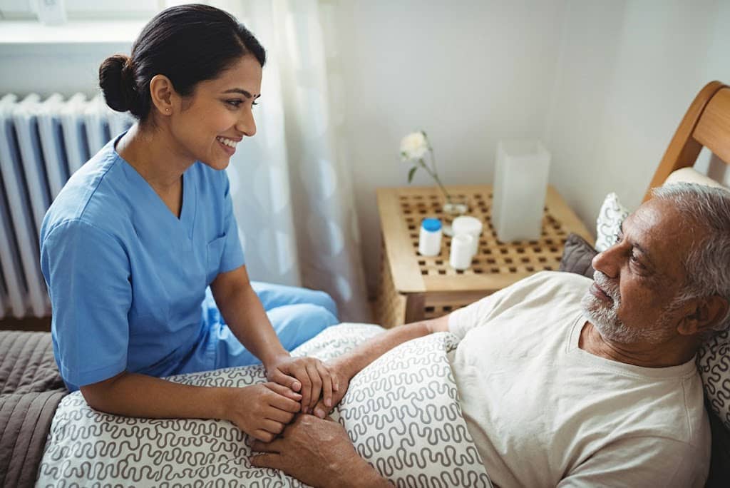 Nurse holding elderly patient's hand providing compassionate palliative care